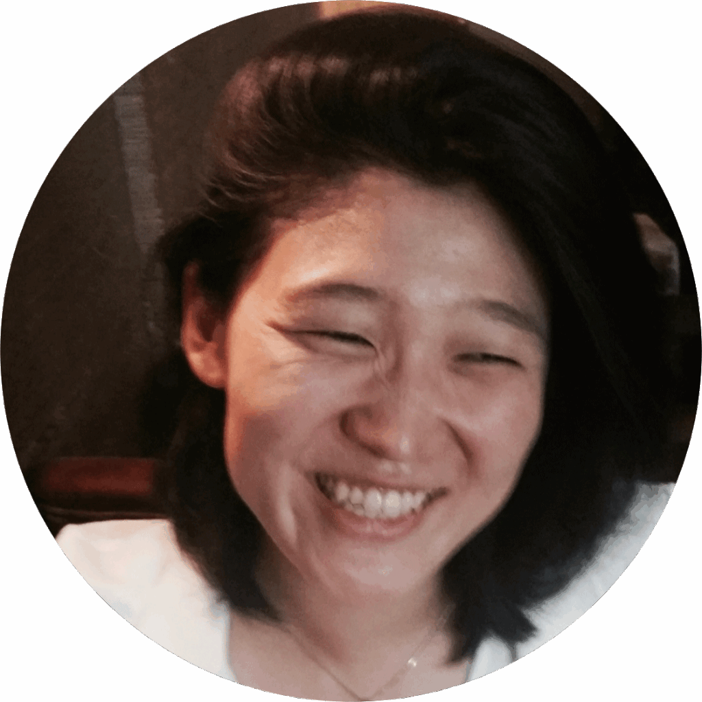 Woman with shoulder-length dark hair smiling, wearing a white top, in a softly lit indoor setting.