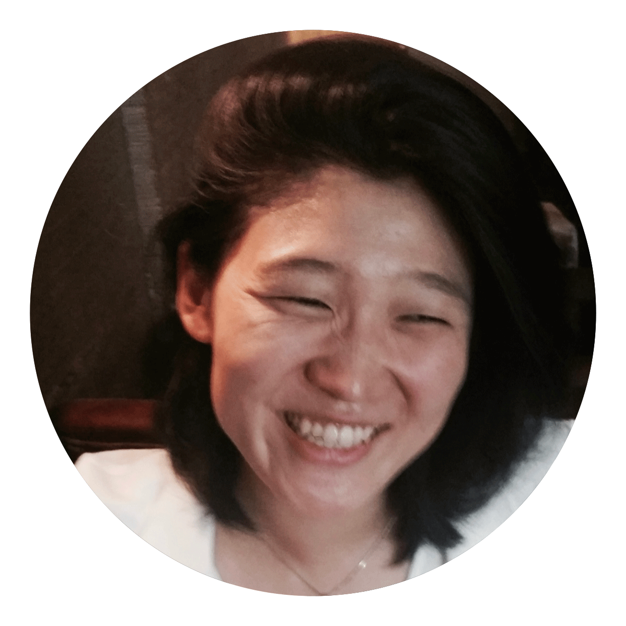 A woman with dark hair is smiling warmly and looking slightly to the side.